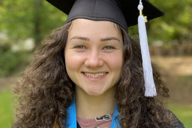 Audrey smiling in cap and gown in front of a blurred background